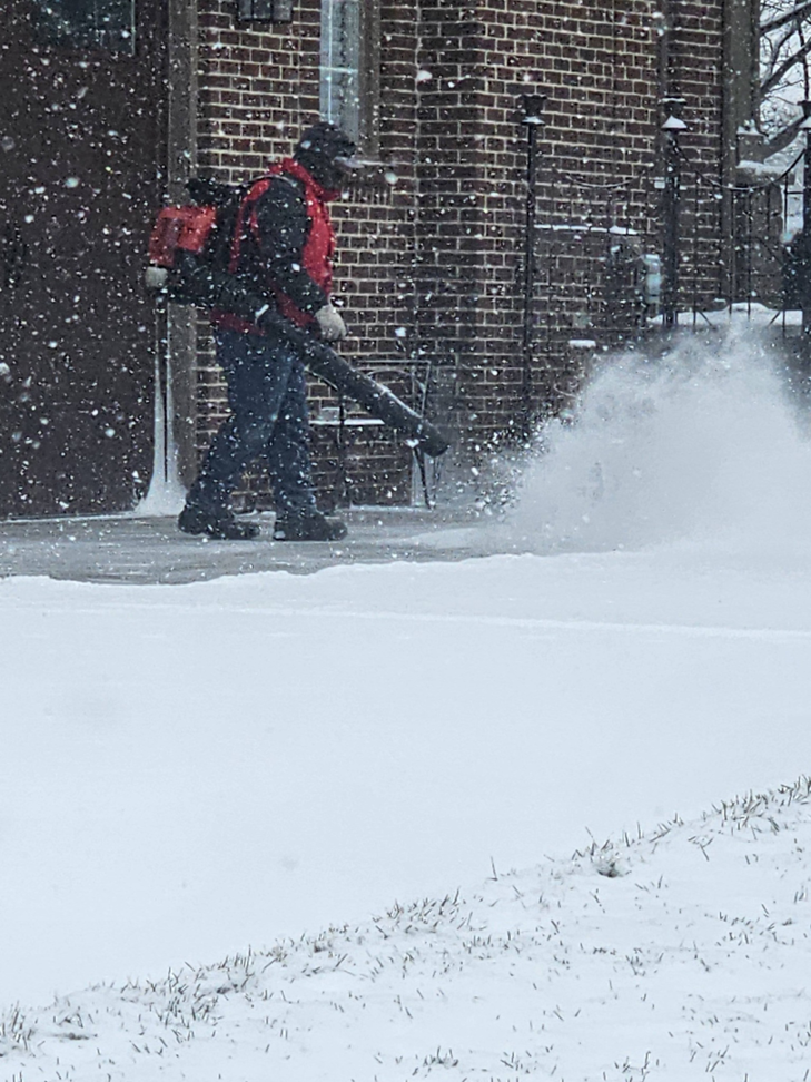 A worker using a backpack blower to clear snow from a sidewalk during a snow removal job by Two brothers landscaping inc. in Fuquay Varina, NC.