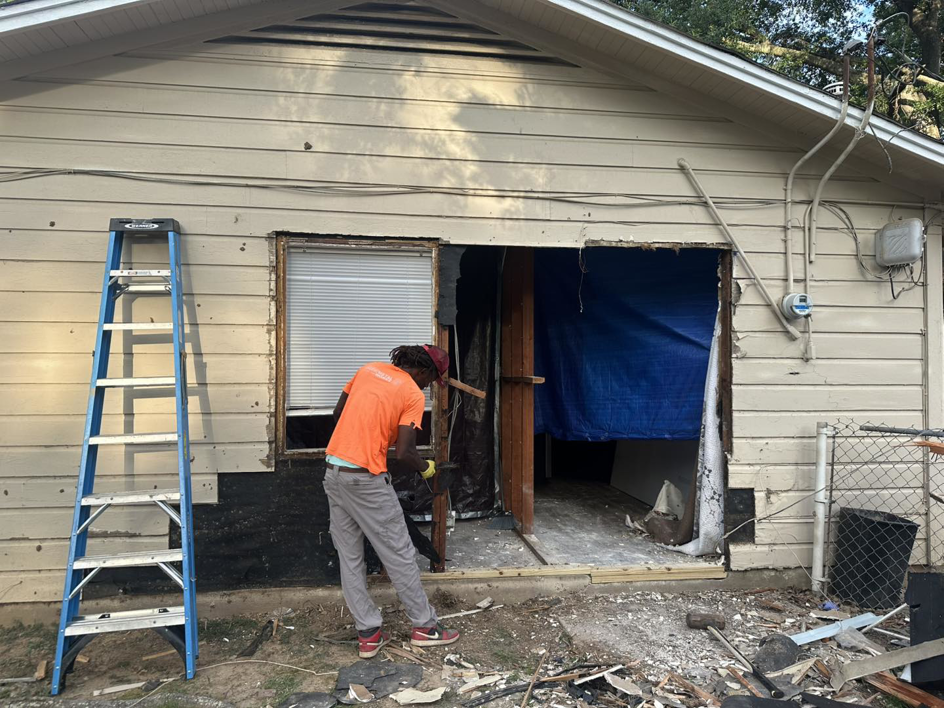 A worker actively demolishing an exterior wall opening at a job site for Rayshawn's Home improvement & Construction work in Bossier City, LA.