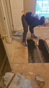 A worker from Restoration Xperts Emergency 24/7 demolishing a water-damaged floor, exposing joists, in Deerfield Beach, FL.
