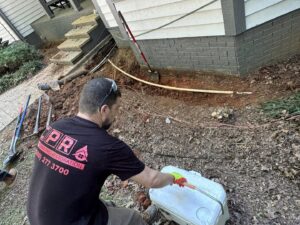 A worker from Carolina Pro Restoration LLC in Fort Mill, SC, digging a trench for foundation drainage or waterproofing.