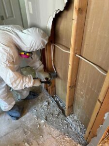A worker in a hazmat suit removing damaged drywall during water damage restoration by RestoPros Hudson County in Jersey City, NJ.