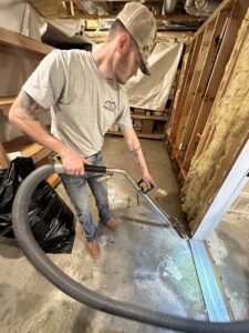 A worker using a water extraction tool on a concrete floor next to exposed wall studs for Utah Home Restoration in Springville, UT
