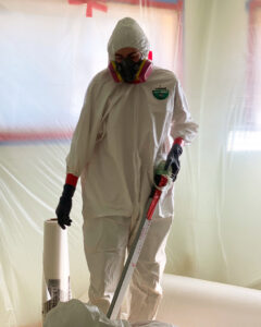 A worker in a hazmat suit within a plastic-sheeted containment area, performing remediation for Central Oregon Disaster Restoration in Bend, OR.