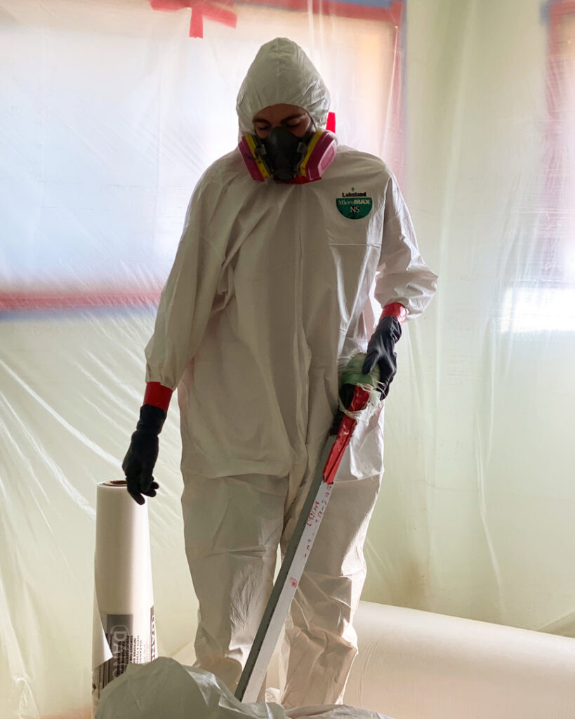 A worker in a hazmat suit within a plastic-sheeted containment area, performing remediation for Central Oregon Disaster Restoration in Bend, OR.