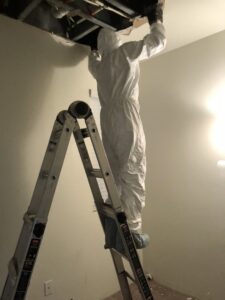 A worker in a white hazmat suit on a ladder inspecting or repairing ceiling damage for Restoration 1 of OKC in Yukon, OK.