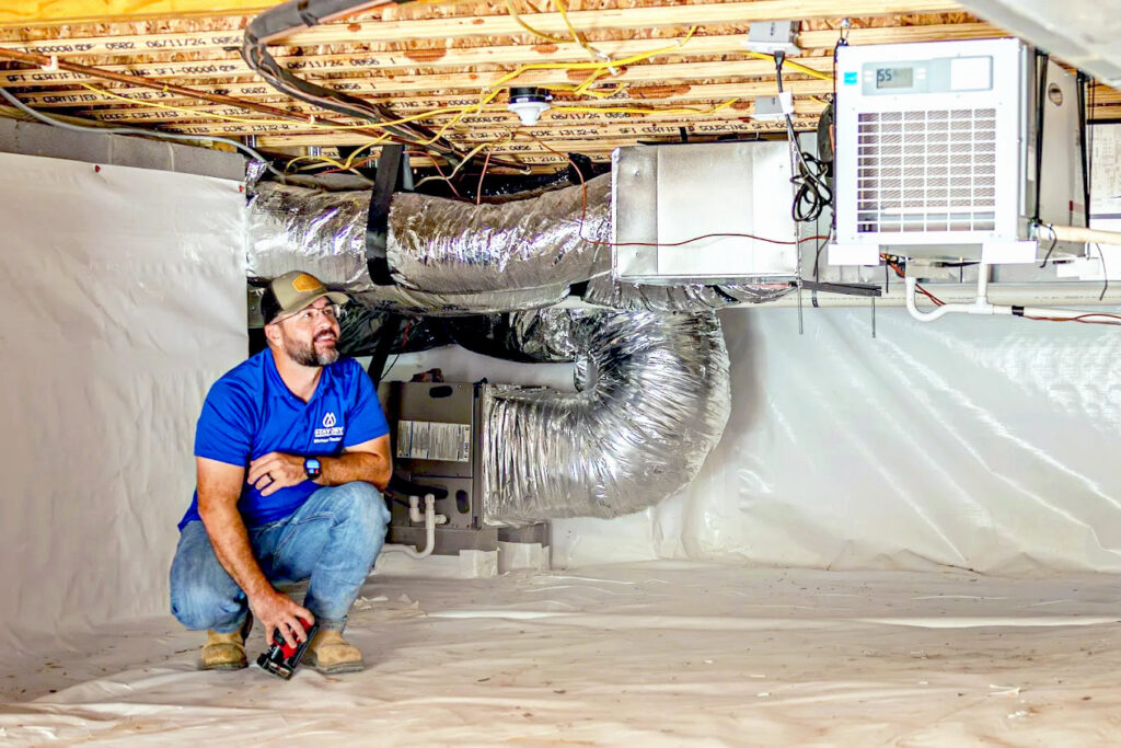 A worker inspecting a newly encapsulated crawl space with a dehumidifier installed by Stay Dry Waterproofing LLC in Marysville, OH.
