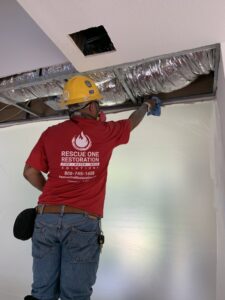 A Rescue One Restoration worker in PPE inspecting an exposed ceiling during mold or water damage remediation in Honolulu, HI.