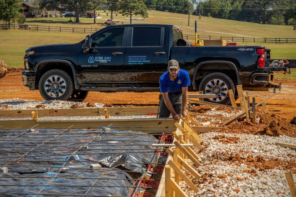 A worker standing in a trench next to a house foundation with newly installed waterproofing membrane by Stay Dry Waterproofing LLC in Marysville, OH.