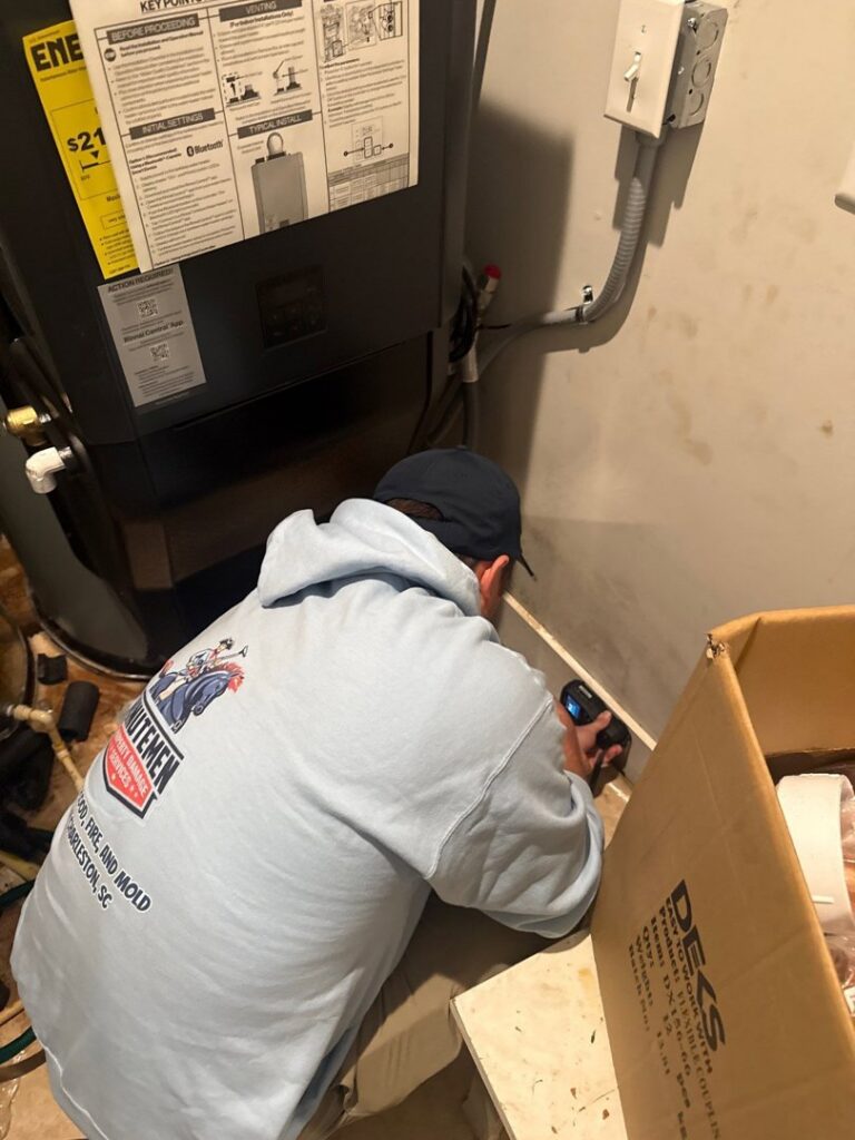 A Minutemen Property Damage Services worker inspecting a wall for moisture near an HVAC unit in North Charleston, SC.