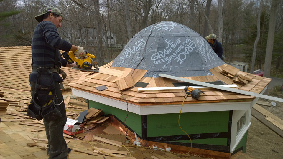 A skilled worker installing cedar shake siding on a house, demonstrating the craftsmanship of JM Roofing & Siding in Rogers, AR.