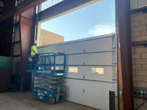 A worker on a scissor lift installing a large commercial garage door for Vertical Door Solutions in Sheridan, WY