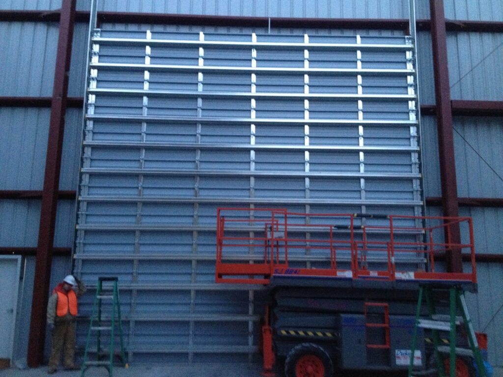 A worker on a scissor lift installing a large commercial garage door inside a building for Alberts Custom Door Company in Wichita, KS.