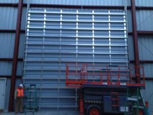 A worker on a scissor lift installing a large commercial garage door inside a building for Alberts Custom Door Company in Wichita, KS.