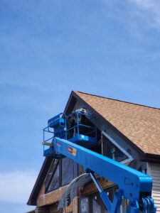 A worker installing siding from a boom lift on a residential home, by Murphy Builders- Genesee County in Ossineke, MI.