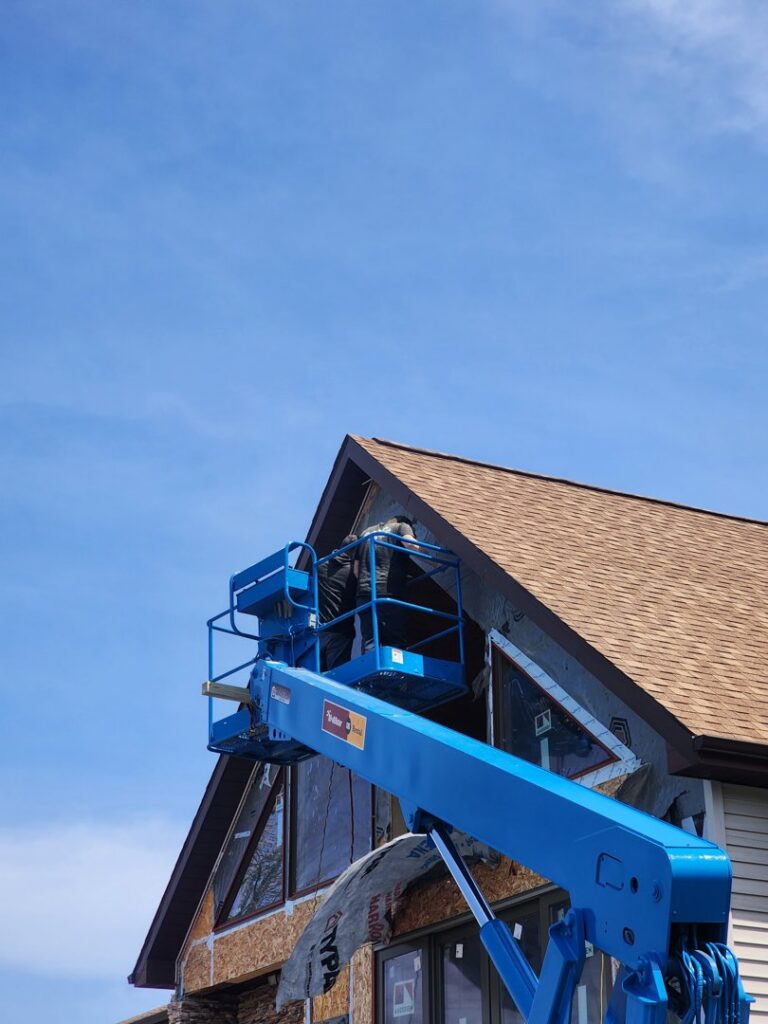 A worker installing siding from a boom lift on a residential home, by Murphy Builders- Genesee County in Ossineke, MI.