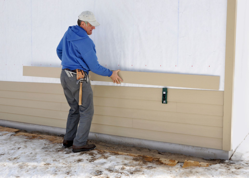 A worker installing tan horizontal siding panels on a house, showcasing a siding contractor job by Arrow Exteriors Inc. in Topeka, KS
