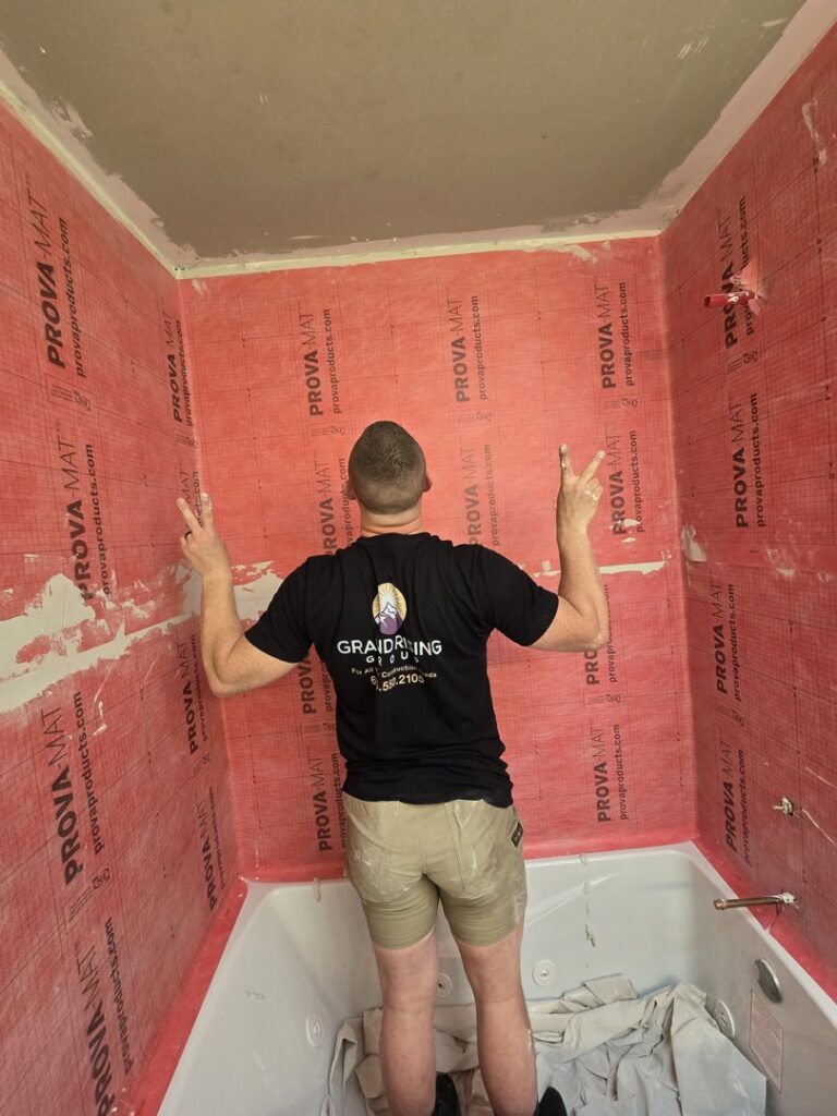 A worker from Grand Rising Group installing a red waterproofing membrane in a bathroom shower area in Mitchell, SD.