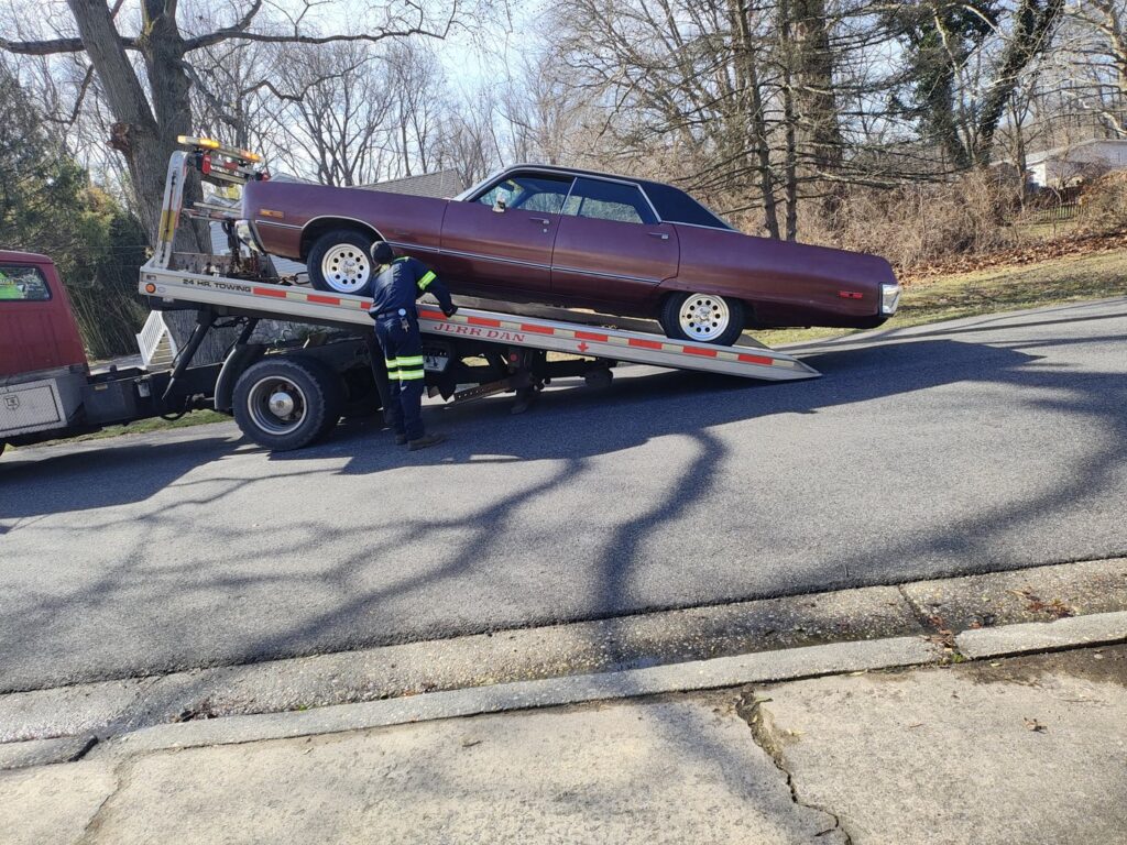 A worker loading a classic maroon car onto a flatbed tow truck for Craig's Towing & Recovery in New Castle, DE.
