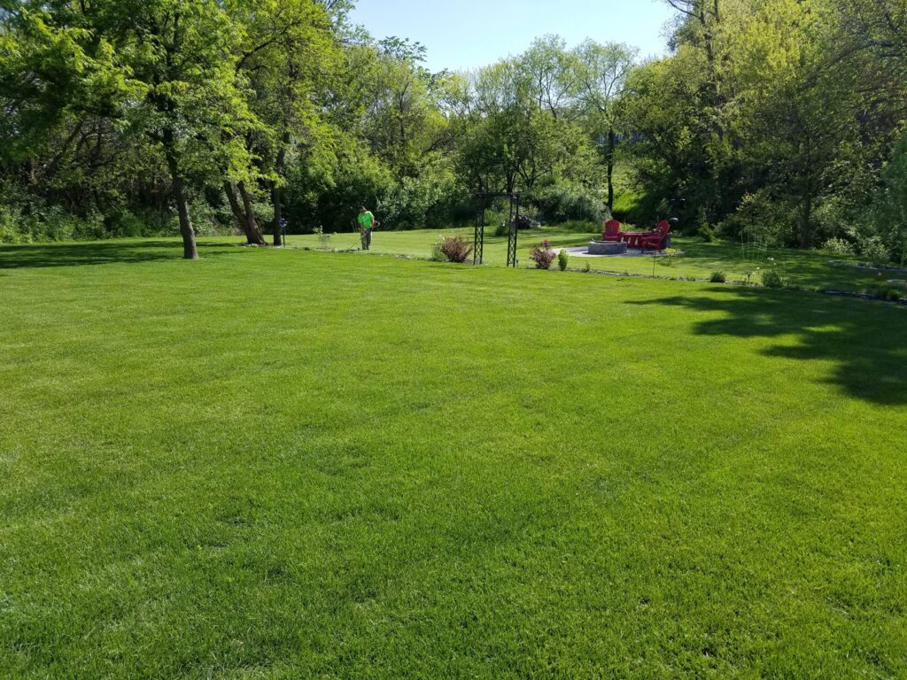 A lawn care professional from Nice & Precise Lawn Care working on a spacious, vibrant green lawn in Ames, IA.
