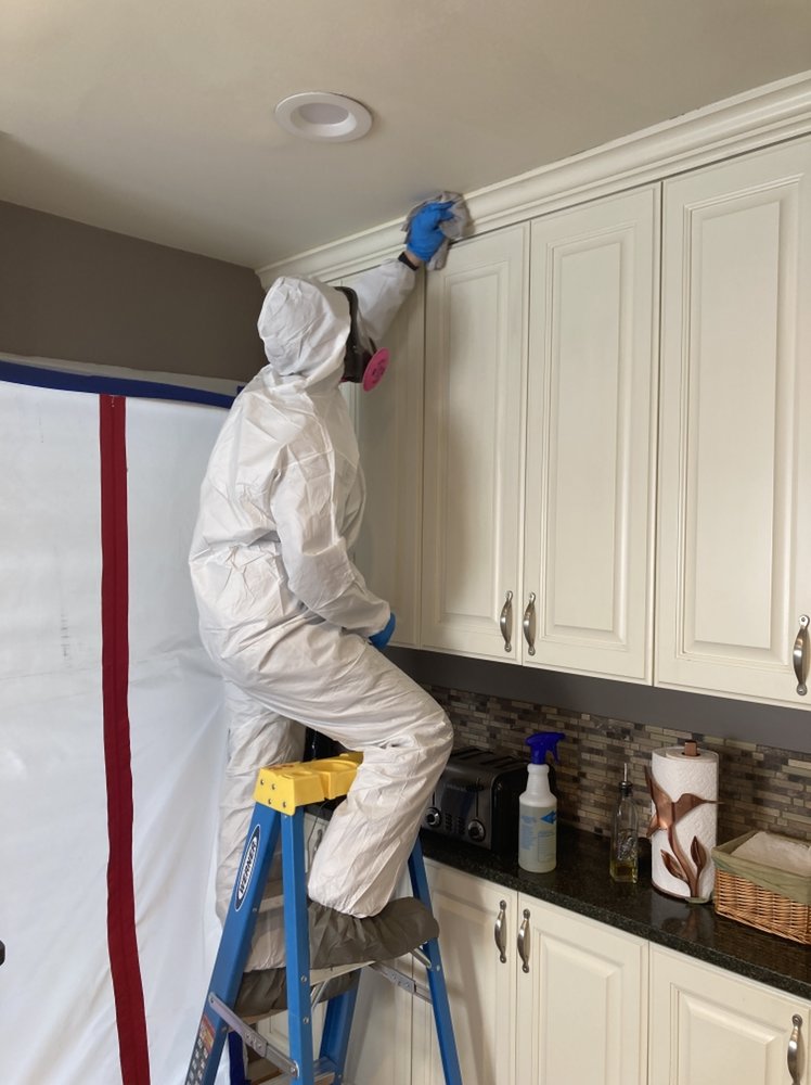 A Flood Pros worker in a hazmat suit and respirator performing remediation work on kitchen cabinets in Sandy, UT.