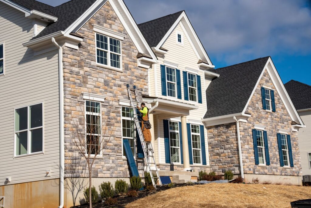 A worker on a ladder installing or repairing siding and shutters on a house exterior, by Jonesboro Siding, Window & Door in Jonesboro, AR.