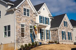 A worker on a ladder installing or repairing siding and shutters on a house exterior, by Jonesboro Siding, Window & Door in Jonesboro, AR.