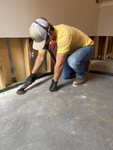 A worker in a respirator preparing a concrete floor next to an exposed wall after water damage by Triangle Restoration in Raleigh, NC.