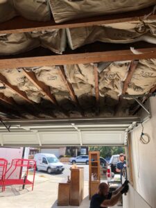 A worker from EZ Water Damage Restoration Services removing damaged drywall and insulation in a garage in Chula Vista, CA.