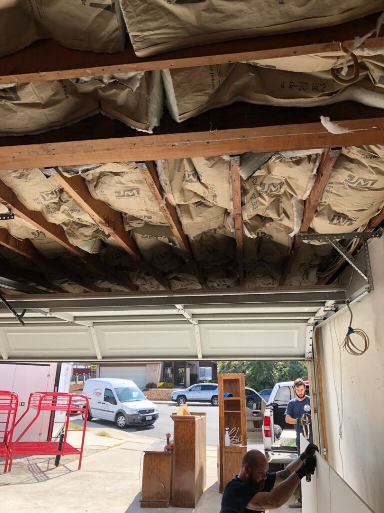 A worker from EZ Water Damage Restoration Services removing damaged drywall and insulation in a garage in Chula Vista, CA.