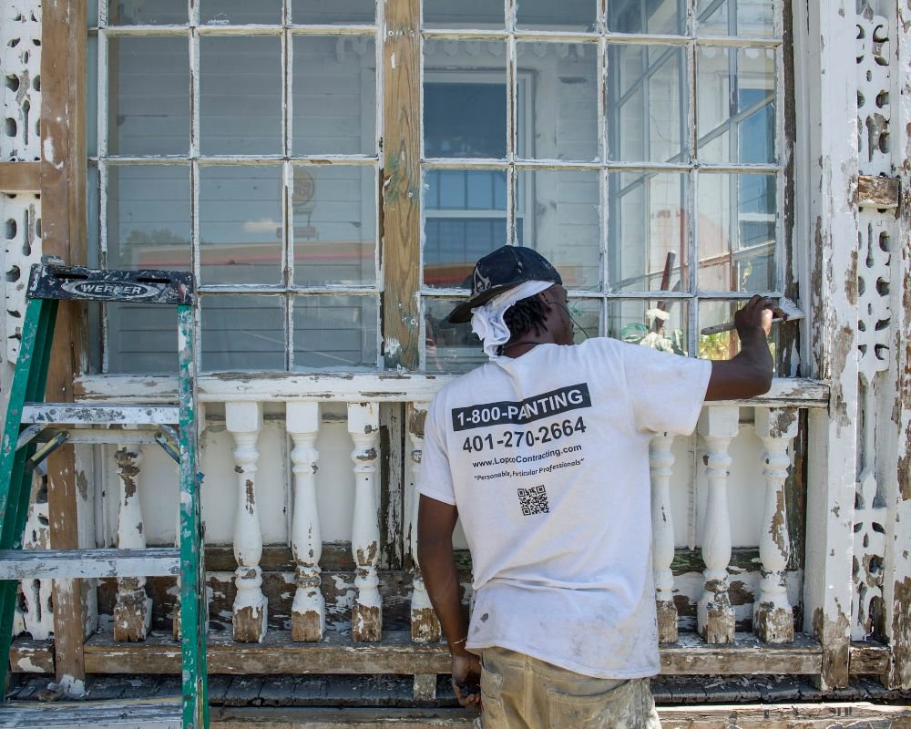 A worker repairing a severely water-damaged window frame on a building exterior for LOPCO Contracting in Johnston, RI.