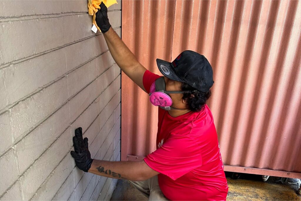 A Rescue One Restoration worker wearing a respirator while cleaning a textured wall, likely for mold remediation in Honolulu, HI.