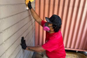 A Rescue One Restoration worker wearing a respirator while cleaning a textured wall, likely for mold remediation in Honolulu, HI.