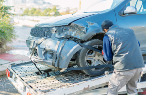 A worker securing a damaged blue car onto a flatbed tow truck for Select Towing and Recovery in Casper, WY.