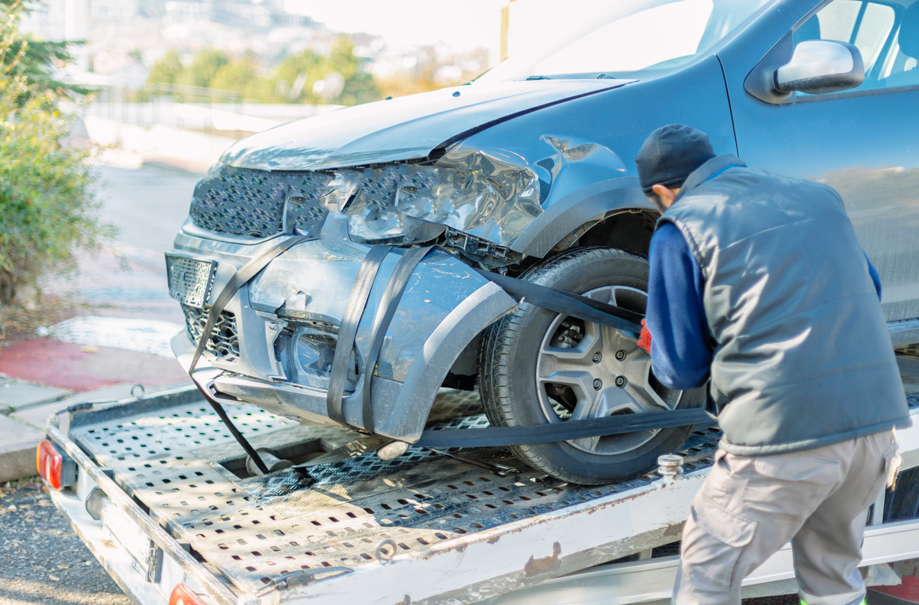 A worker securing a damaged blue car onto a flatbed tow truck for Select Towing and Recovery in Casper, WY.
