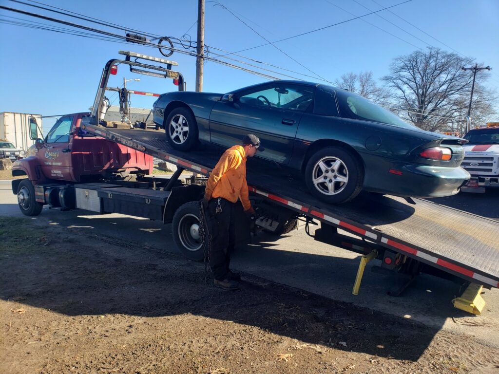 A worker securing a green sports car onto a flatbed tow truck for Craig's Towing & Recovery in New Castle, DE.