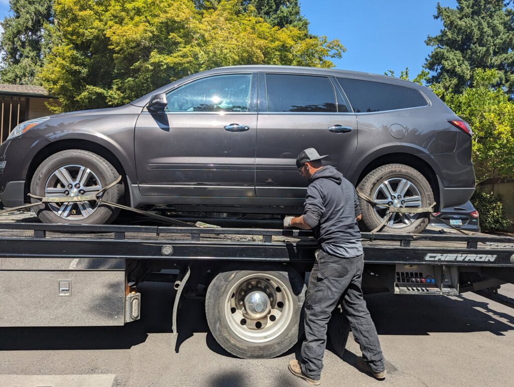 A tow truck operator securing a grey SUV onto a flatbed tow truck for Speed's Towing in Vancouver, WA.