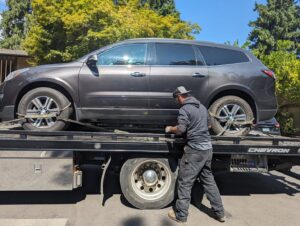 A tow truck operator securing a grey SUV onto a flatbed tow truck for Speed's Towing in Vancouver, WA.