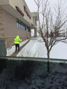 A worker from TLC Lawn Care and Snow Removal LLC shoveling snow from a sidewalk in front of a Walgreens in Colorado Springs, CO.