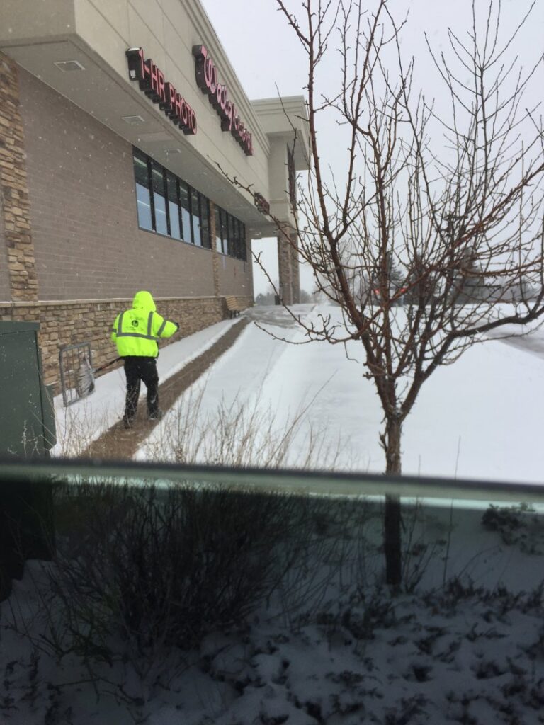 A worker from TLC Lawn Care and Snow Removal LLC shoveling snow from a sidewalk in front of a Walgreens in Colorado Springs, CO.