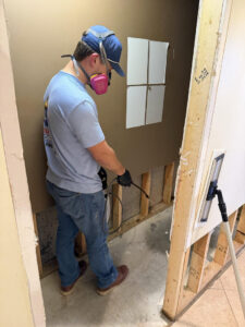 A worker in a respirator spraying a solution on a wall during mold or water damage remediation by Triangle Restoration in Raleigh, NC.