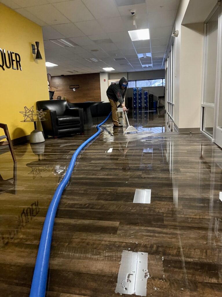 A worker using a squeegee to remove standing water from a floor, a service of Central Oregon Disaster Restoration in Bend, OR.