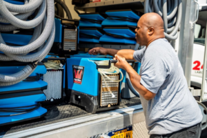 A Claim Masters worker unloading a Phoenix Dry Max dehumidifier from a service truck for a water damage job in New Hartford, NY.