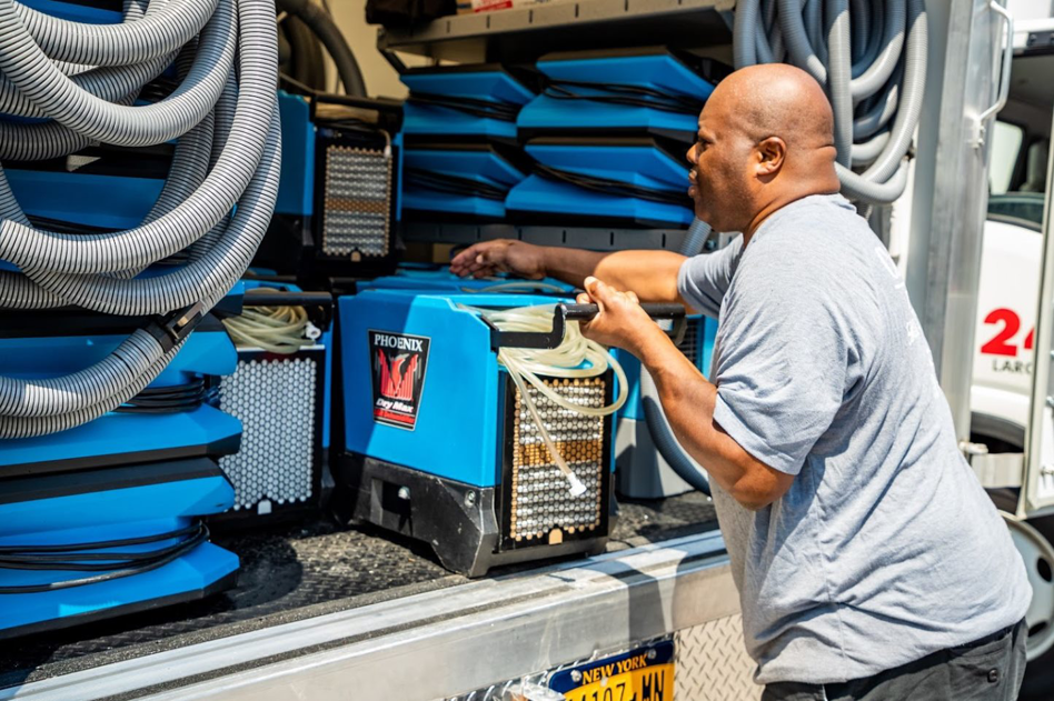 A Claim Masters worker unloading a Phoenix Dry Max dehumidifier from a service truck for a water damage job in New Hartford, NY.