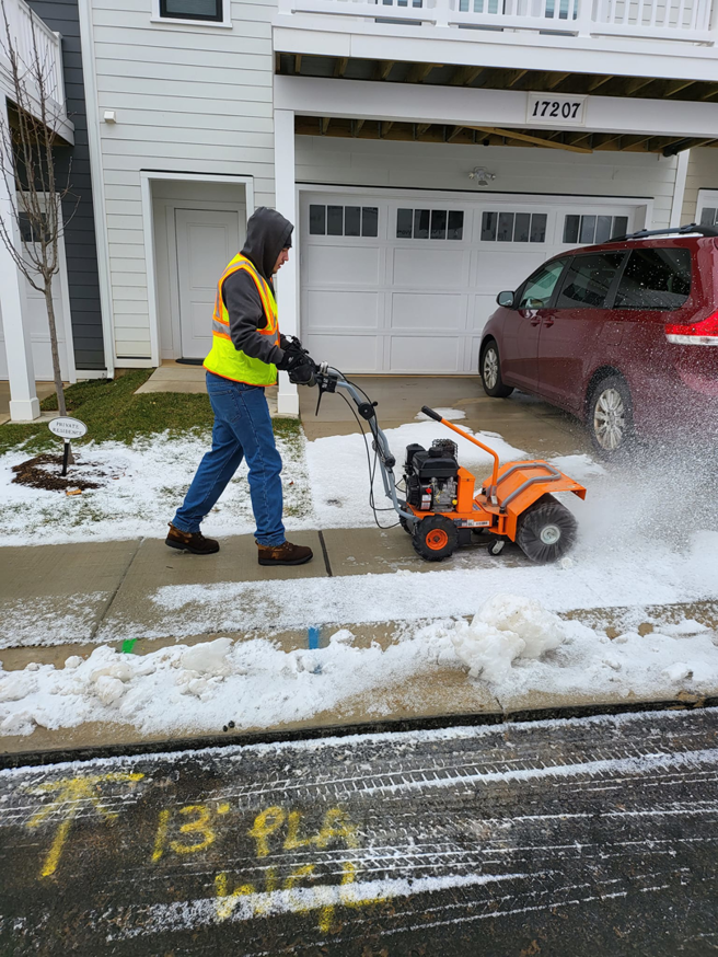 A worker operating a walk-behind snow blower to clear snow from a sidewalk for American Snow Plowing Services in Rockville, MD.
