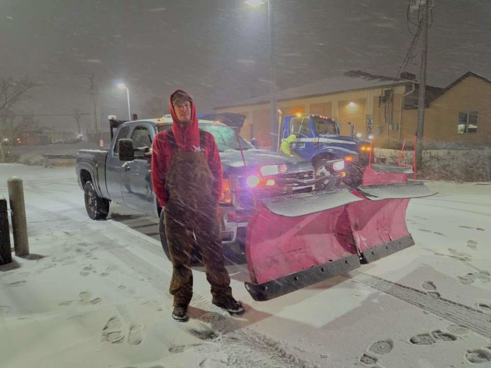 A worker standing in front of a pickup truck with a snow plow attached at night for Eric's Winter & Landscape Services in Appleton, WI