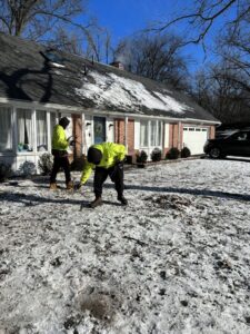 Two workers from Cox's Tree and Lawn Care LLC clearing patchy snow from a residential lawn in Toledo, OH.