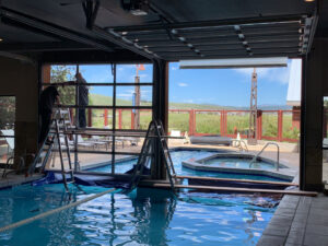 Workers from Canyon Overhead Doors installing a glass garage door next to an indoor pool in Salt Lake City, UT.