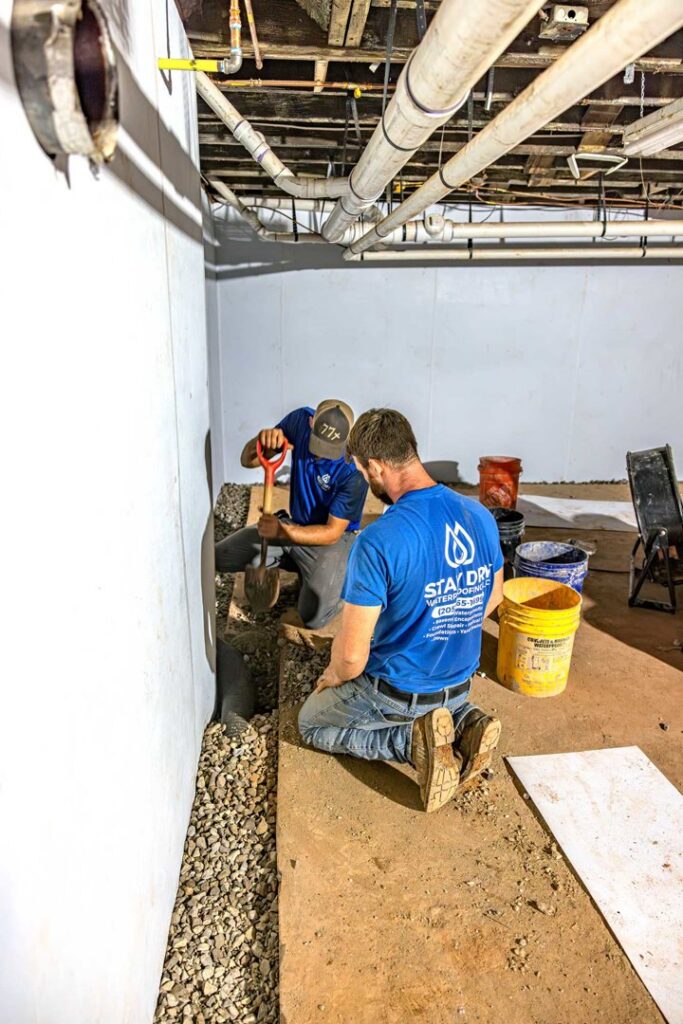 Two workers installing an interior drainage system in a basement to prevent water damage by Stay Dry Waterproofing LLC in Marysville, OH.