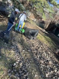 Two workers performing leaf cleanup with rakes and a ride-on mower for Top Cut Lawn Care and Snow Removal in Minot, ND.