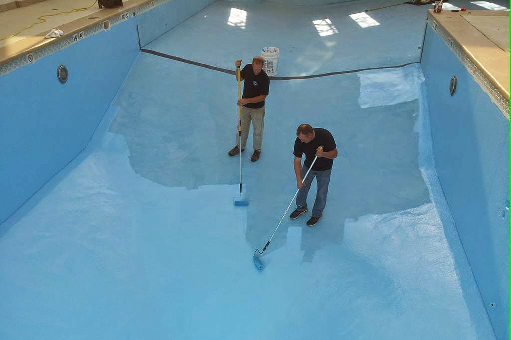 Two workers painting the interior surface of an empty swimming pool for Platinum Pools in Houston, TX